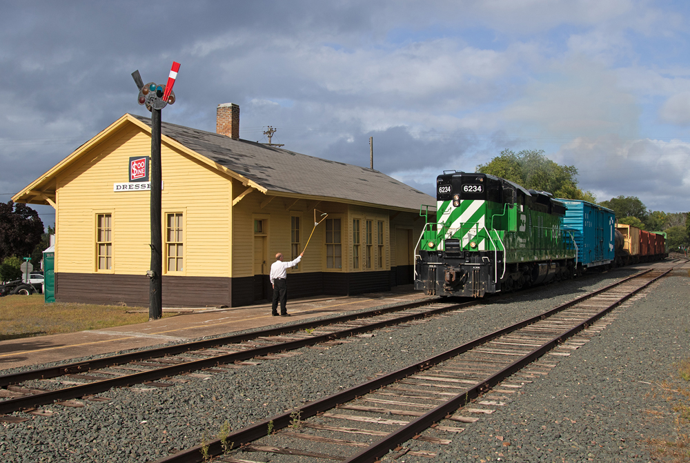 green diesel next to yellow depot with man handing off train orders