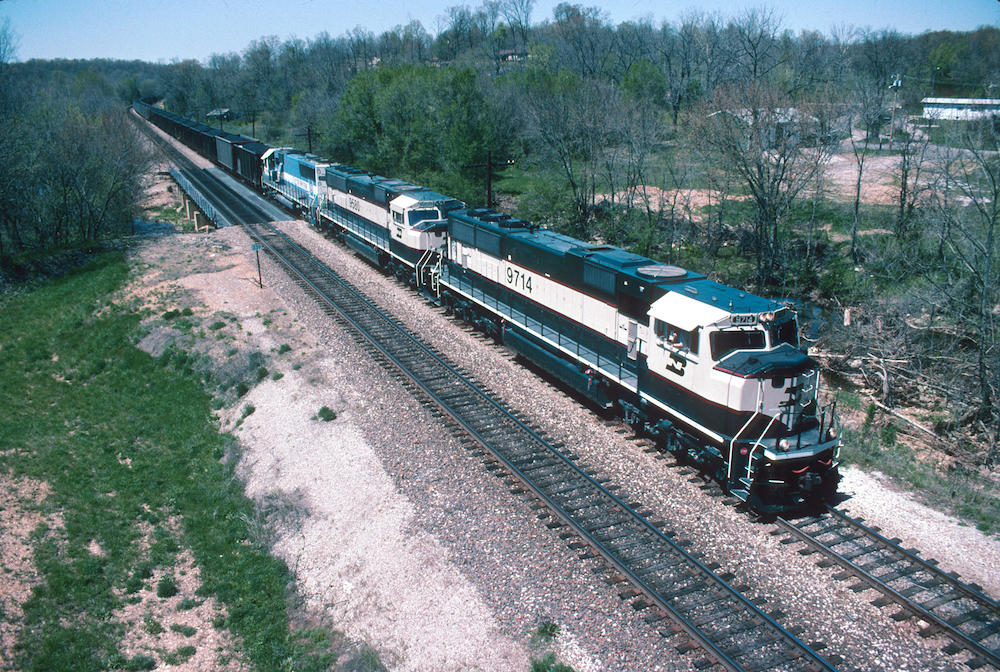 Dark green with cream striped locomotives with a green field in the foreground and scattered trees in the backfround