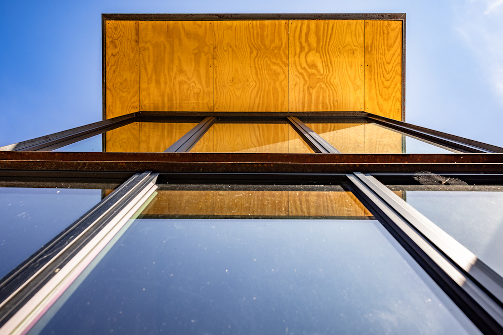 A image with the camera pointed toward the blue sky showing a two-story glass wall and overhanging roof.