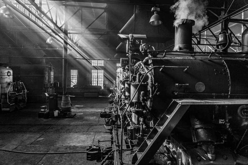 Black and white photo inside a railroad shop with steam and diesel locomotives. Nevada Northern Railway Museum to host Iron Horse Symposium.