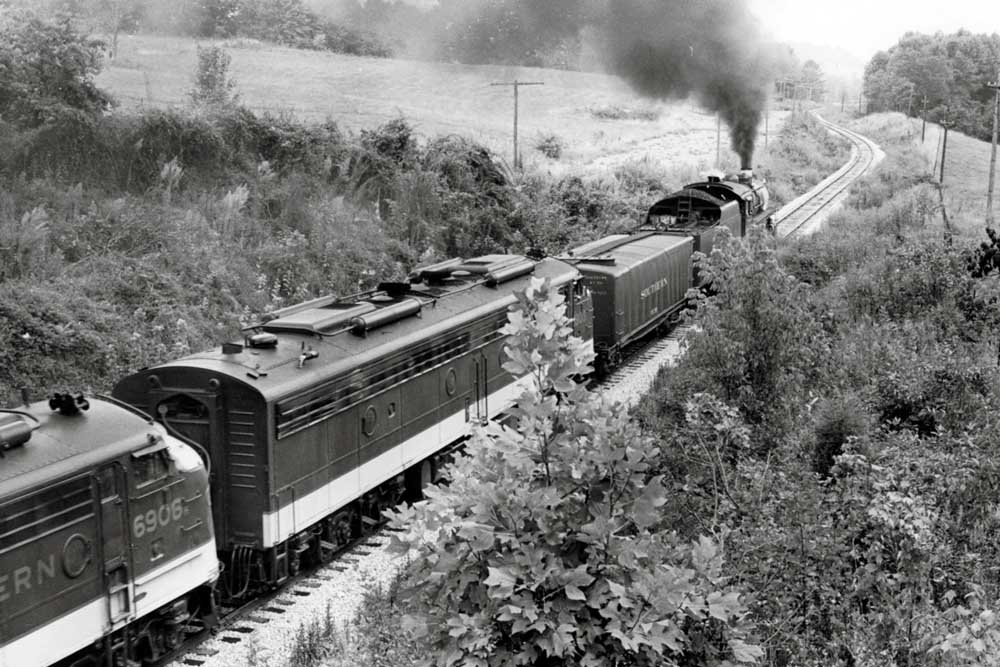 Steam locomotive leads passenger train around curve behind trees