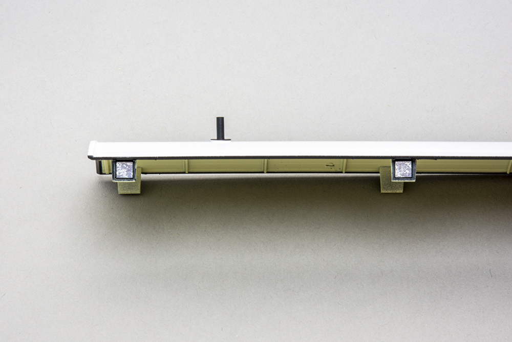 Side view of a white model roof for a British train wagon showing two silver metallic tabs containing magnets.
