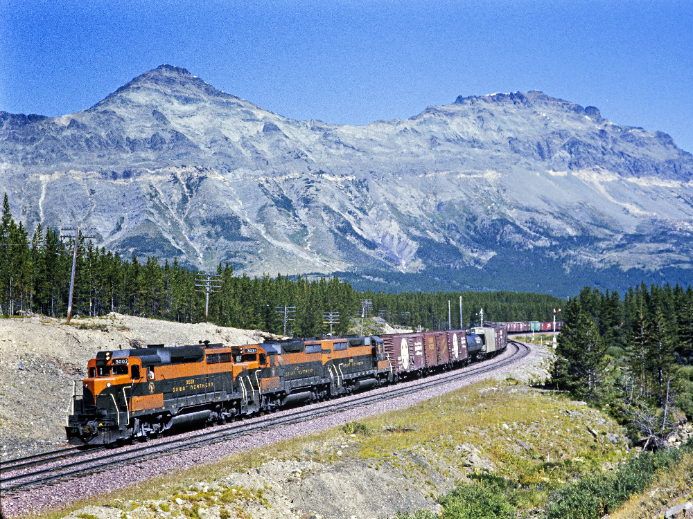 Orange and green locomotives pulling a freight train through the mountains. CRP&A received $1 million endowment contribution.
