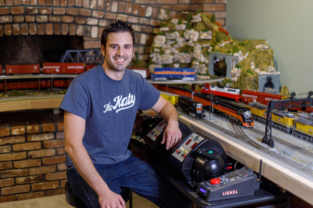 young man sitting next to train layout