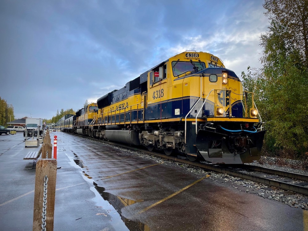 A yellow and blue passenger train rest beside a rain-soaked platform. Alaska by Rail adventure