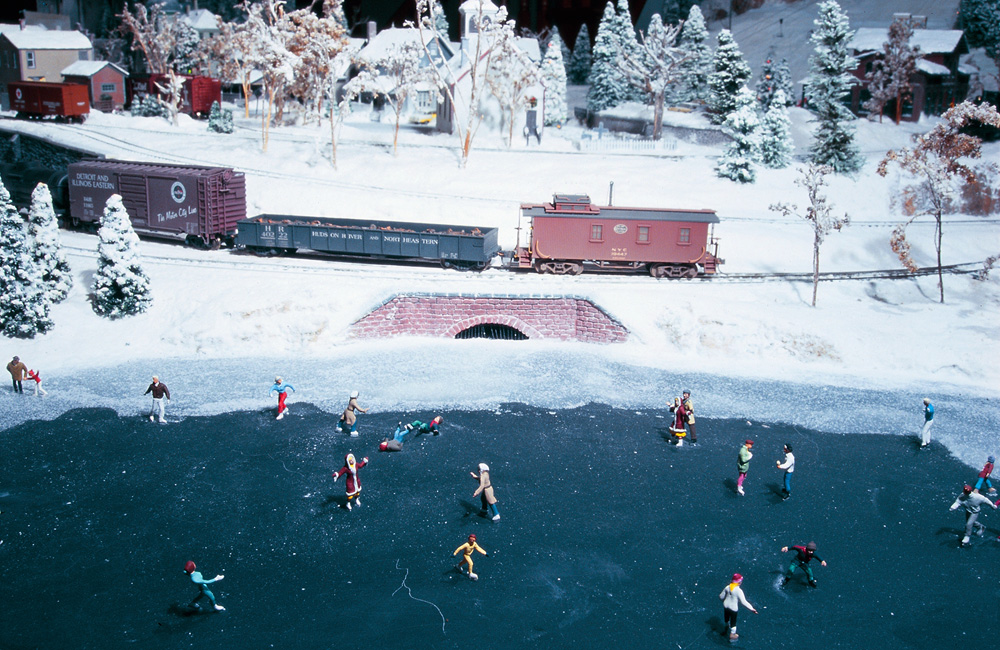 The tail end of a freight train rolls past a frozen pond with ice skaters