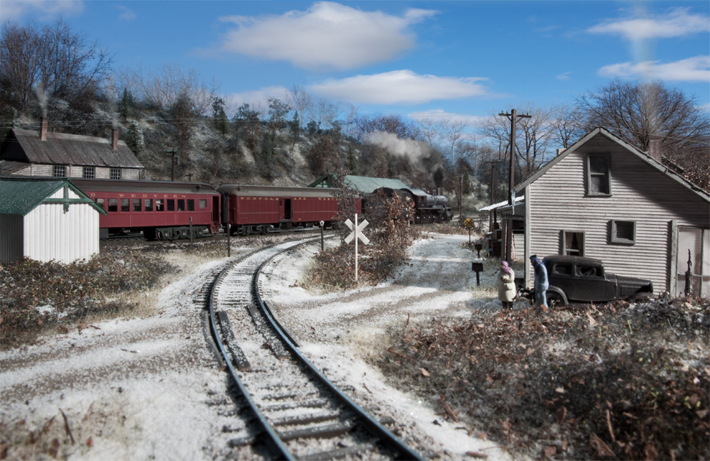 A dusting of snow lies across the track as a passenger train rolls by in the distance
