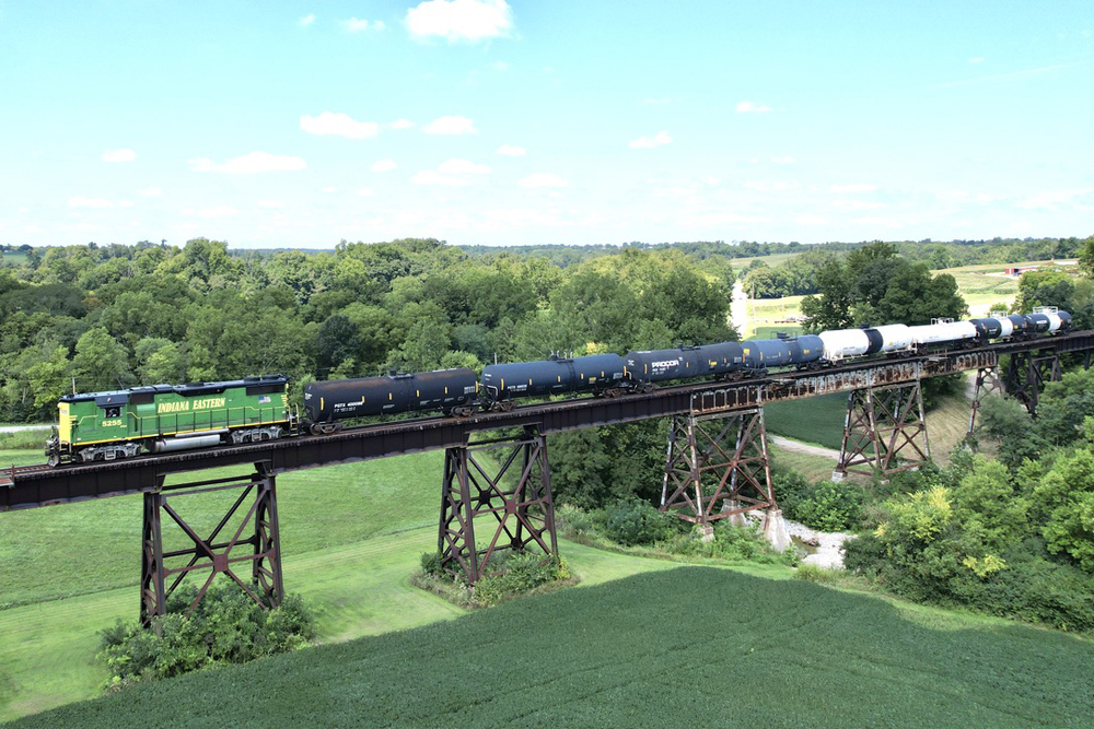 Green and yellow locomotive with freight train on trestile