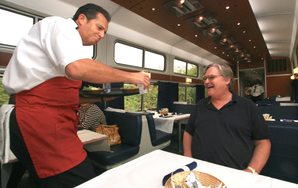 Man in red apron serving to customer at table.