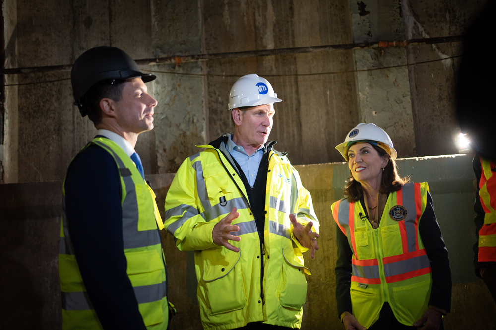 Three people in hard hats and hi-visibility vests in construction area