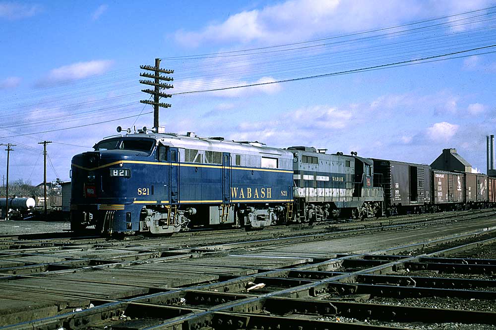 Two blue-and-gray diesel Wabash locomotives on freight train crossing railroad tracks