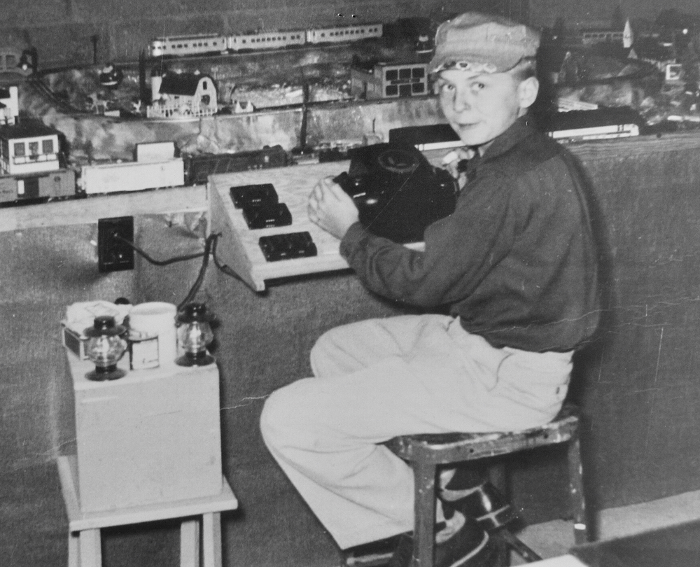 black and white photo of boy next to train layout