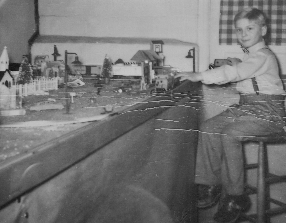 black and white photo of boy next to train layout