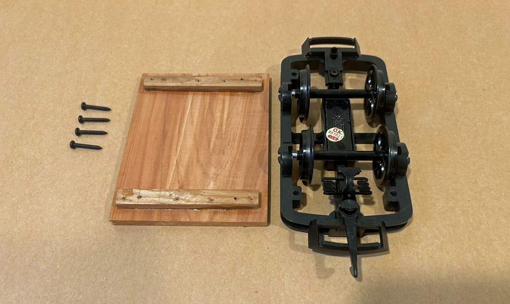 black model chassis next to piece of wood and four screws