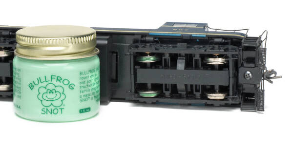 A small jar of opaque green liquid sits next to a model locomotive with two of its wheels showing green treads