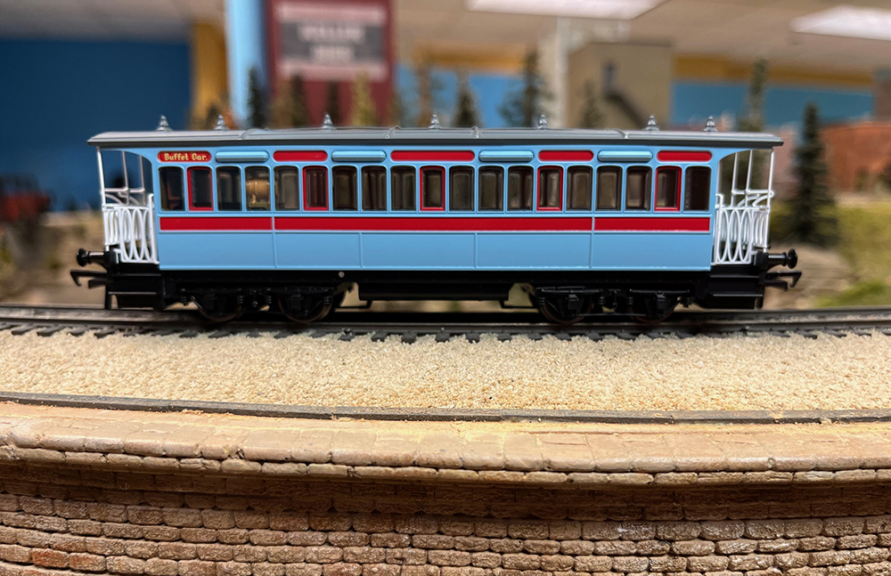 Gray, red, and black model train passenger car on tan stone bridge