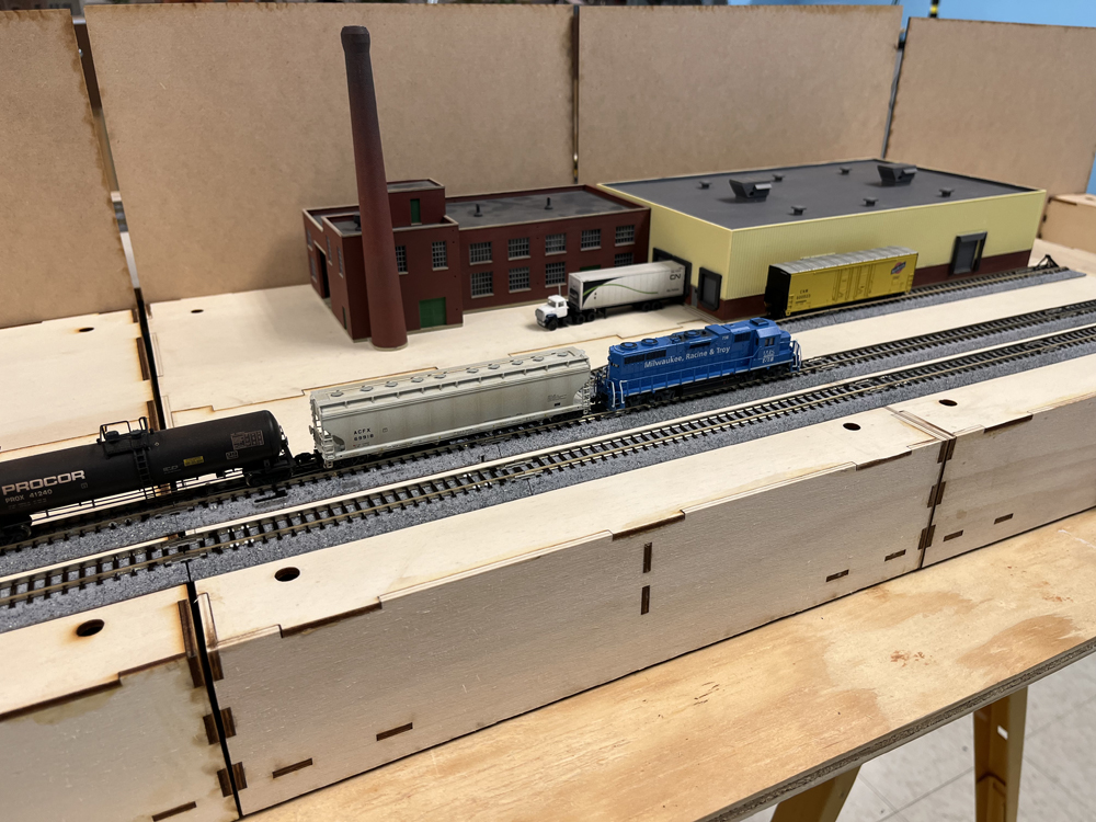 Model railroad module with warehouse on it on top of plywood base
