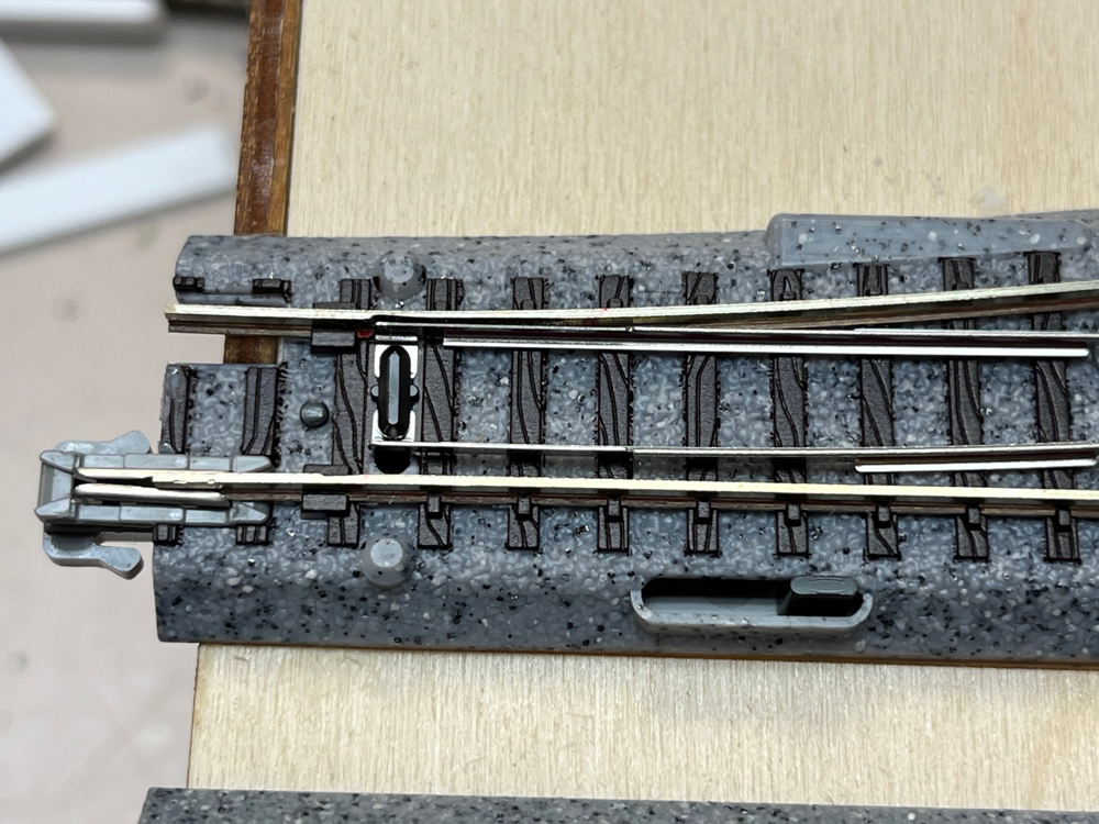 Bright metal model train rail on black and gray plastic roadbed.