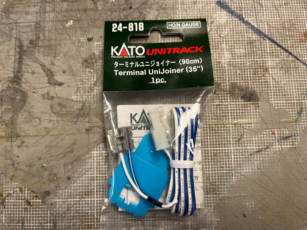 Clear package with green and white label containing blue and white wires attached to small gray plastic blocks and a blue hex-shaped piece of plastic.