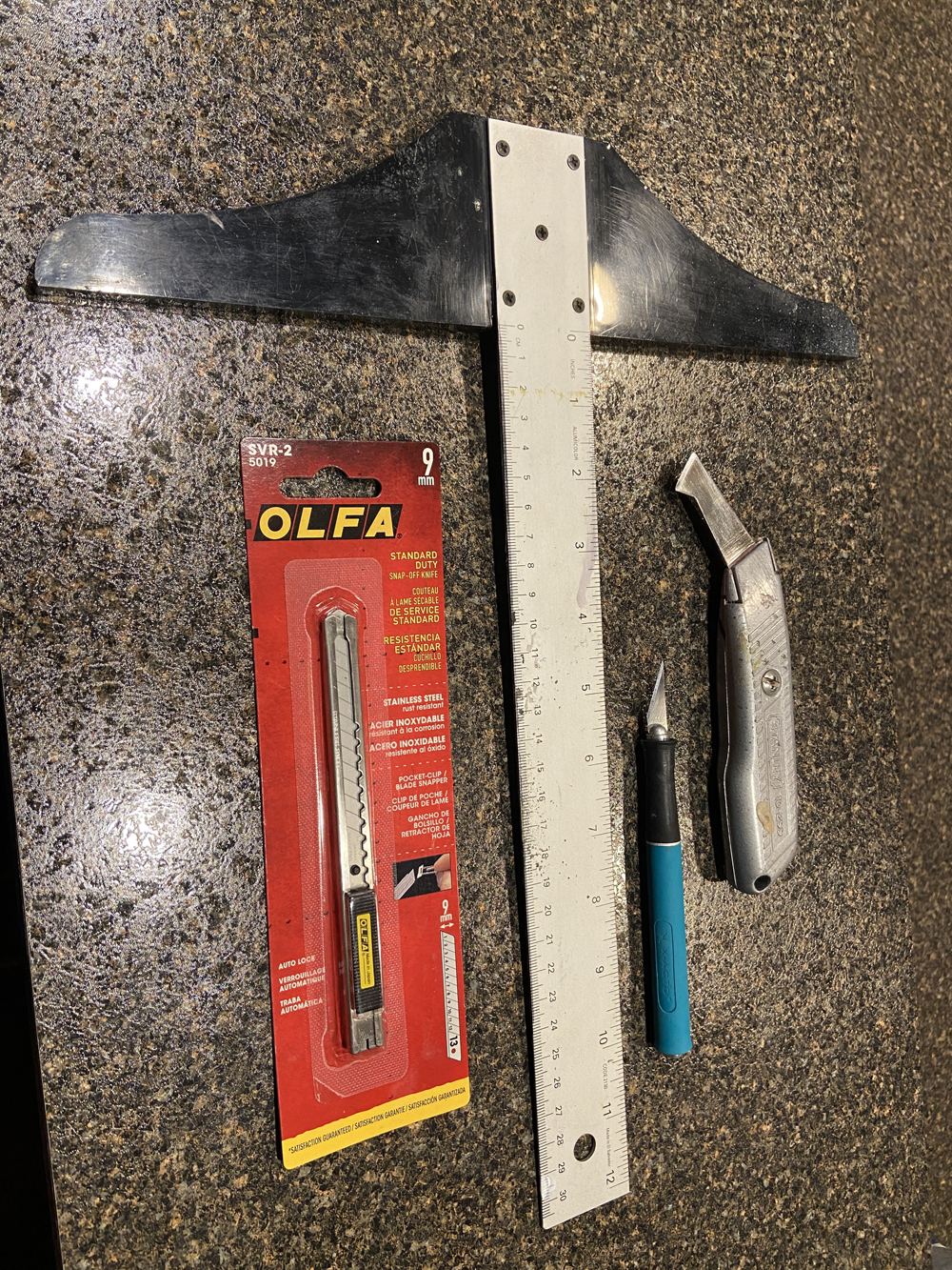 A T-square, razor knife, X-Acto knife, and scoring knife on a table