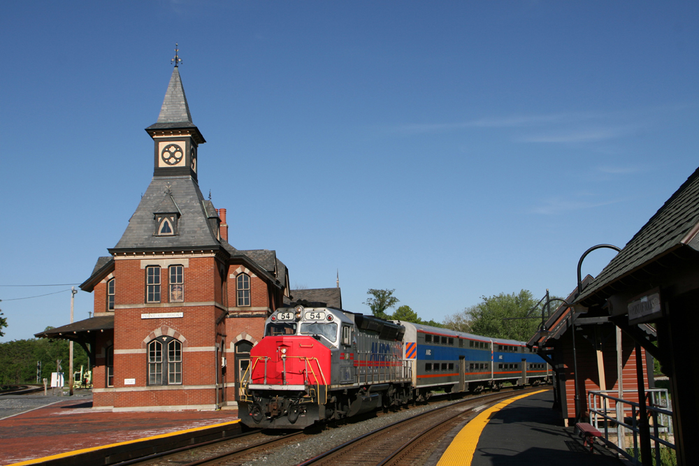 Red and silver passenger train passing red-brick station.