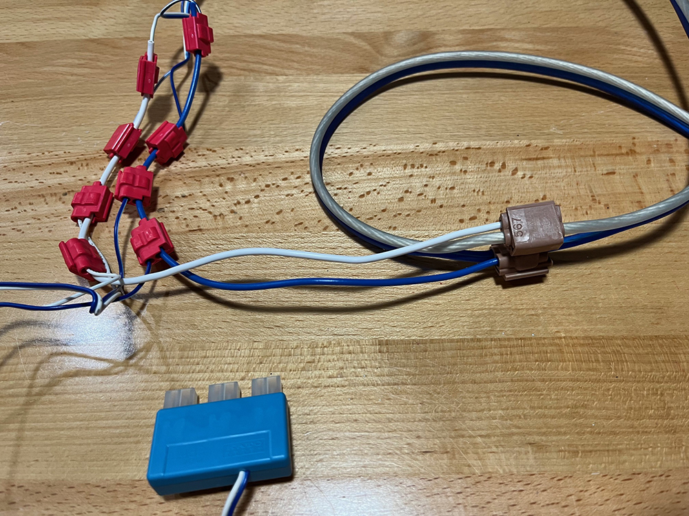Blue and white wires with small brown and red boxes attached resting on bare wood surface.