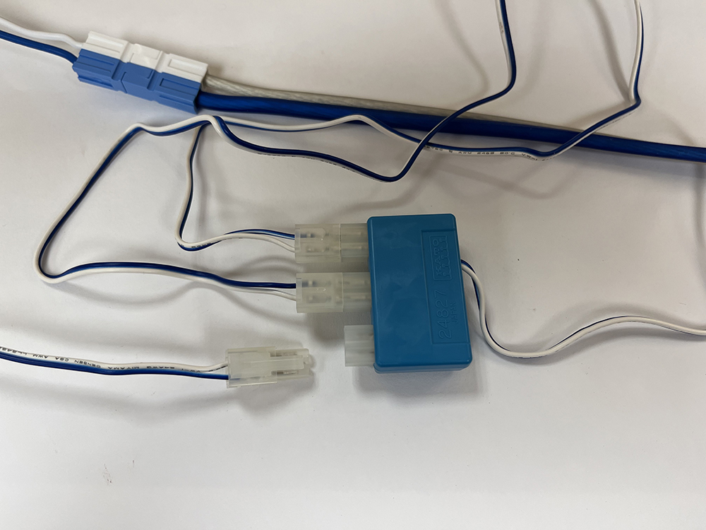 Blue rectangular box with clear plugs and sockets attached to assorted blue and white wires on a white background.