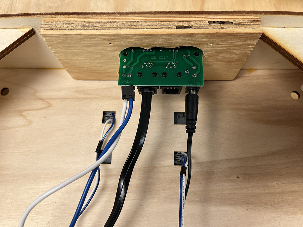 Green circuit board mounted to wood box with assorted colored wire connections to it.