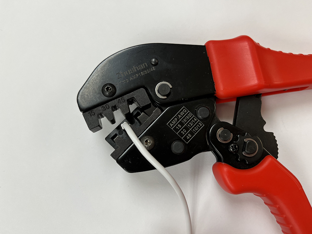 Red and black pliers with jaws open holding a white wire on a white background.