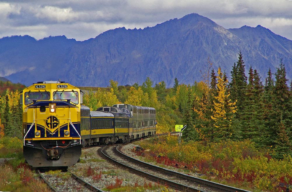 Blue and yellow passenger train with mountains in the background.