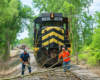 Black locomotive with yellow stripes and men moving tree