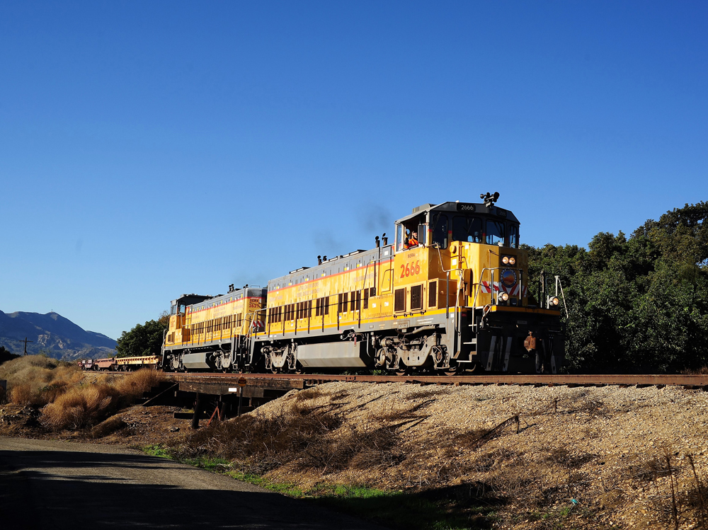 yellow locomotive on train track with clear blue skies