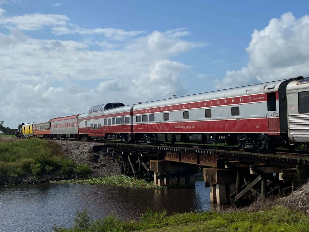 Vintage passenger cars cross a bridge over a creek.