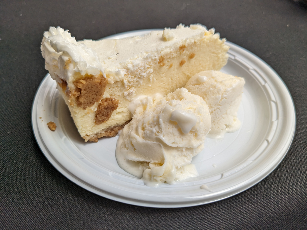 A slice of cheesecake and two scoops of vanilla ice cream on a plate.