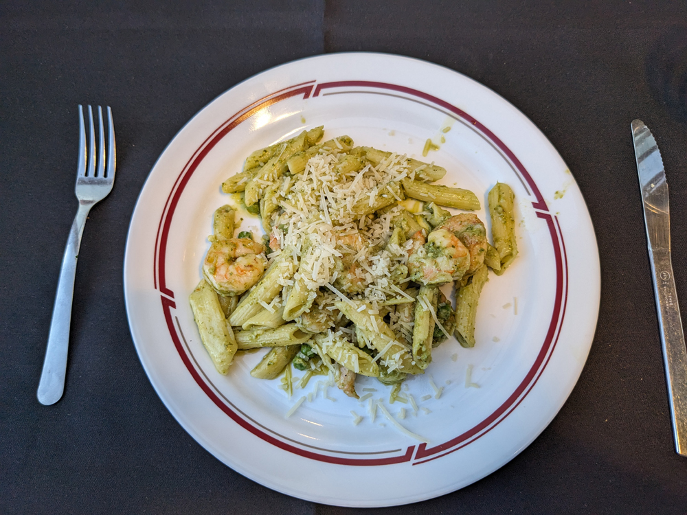 Shrimp pesto pasta on a plate with fork and knife.