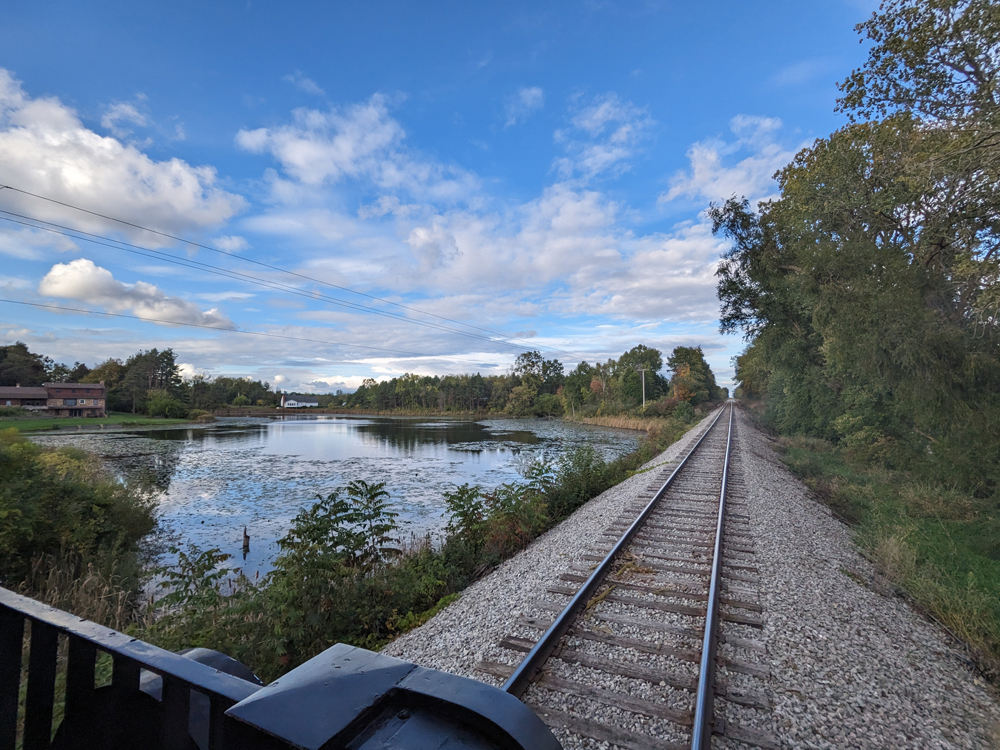 A pond and the sky are seen from the back platform of a private car.