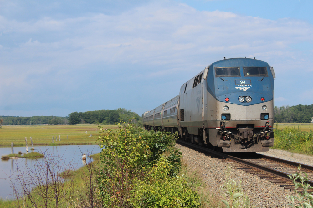 Passenger train passes next to small body of water