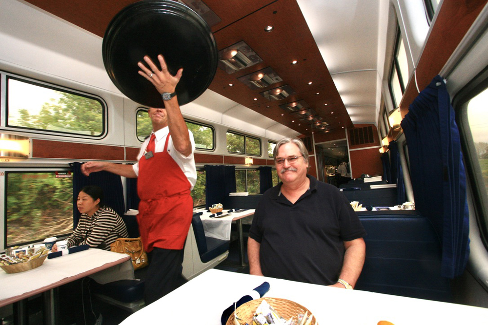 Server in diner holding serving tray high above table as he moves down aisle