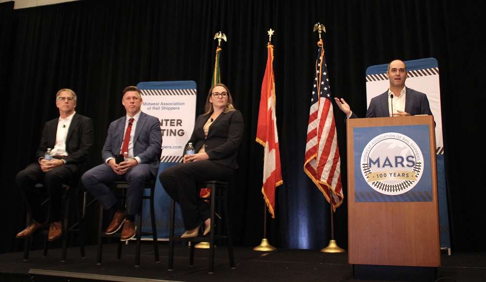 Three people on chairs and man at podium on stage