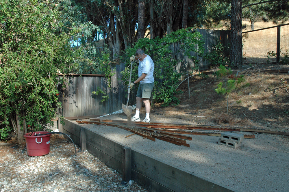 man standing outdoors next to in-progress garden railroad