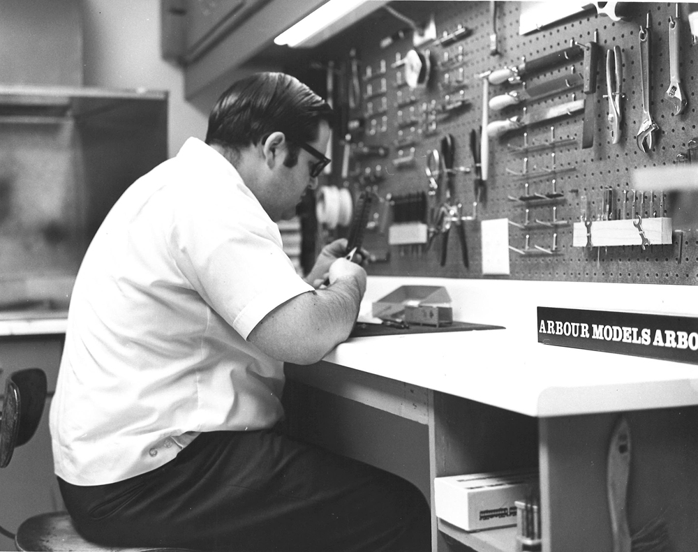 Black-and-white photo of man building a model at a workbench.