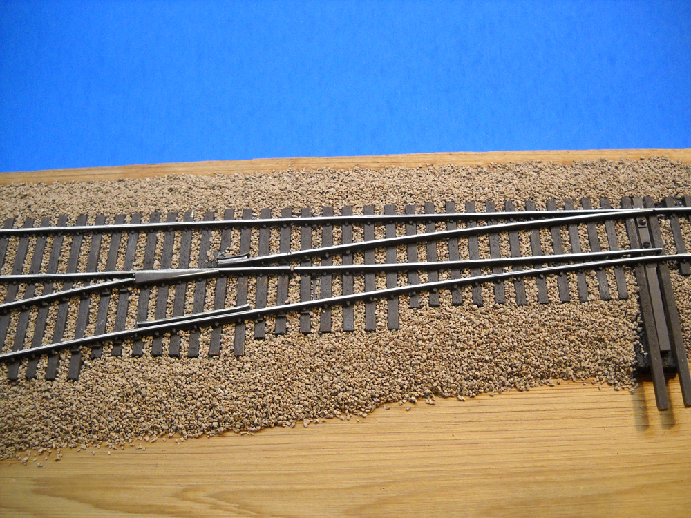 A model train lift-frog turnout, ballasted with a blue background