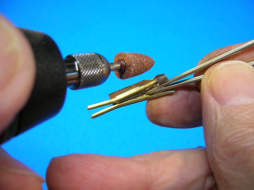 A motor tool next to fingers holding a model railroad turnout frog