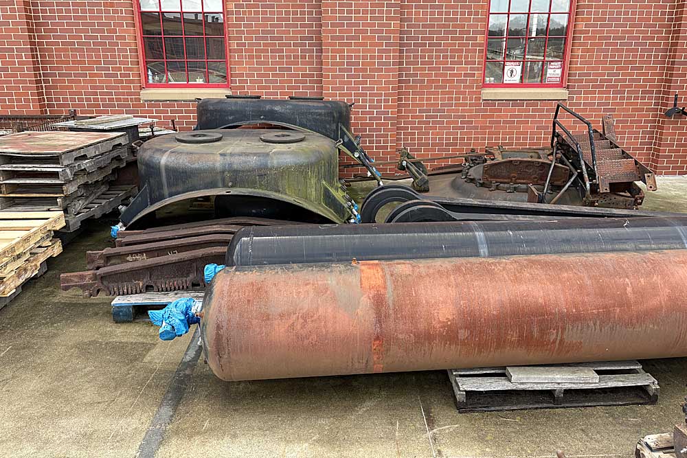 Rusted steam locomotive parts outside brick building