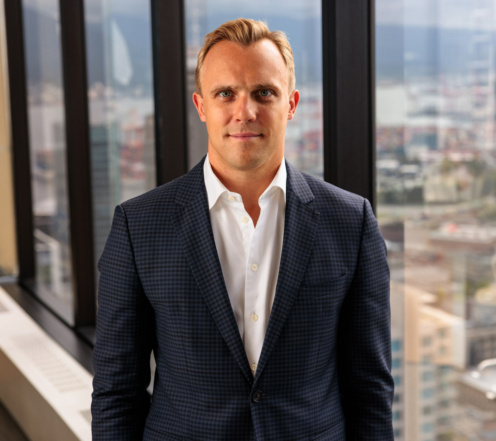 Man in sportcoat and white shirt with city visible through window in background
