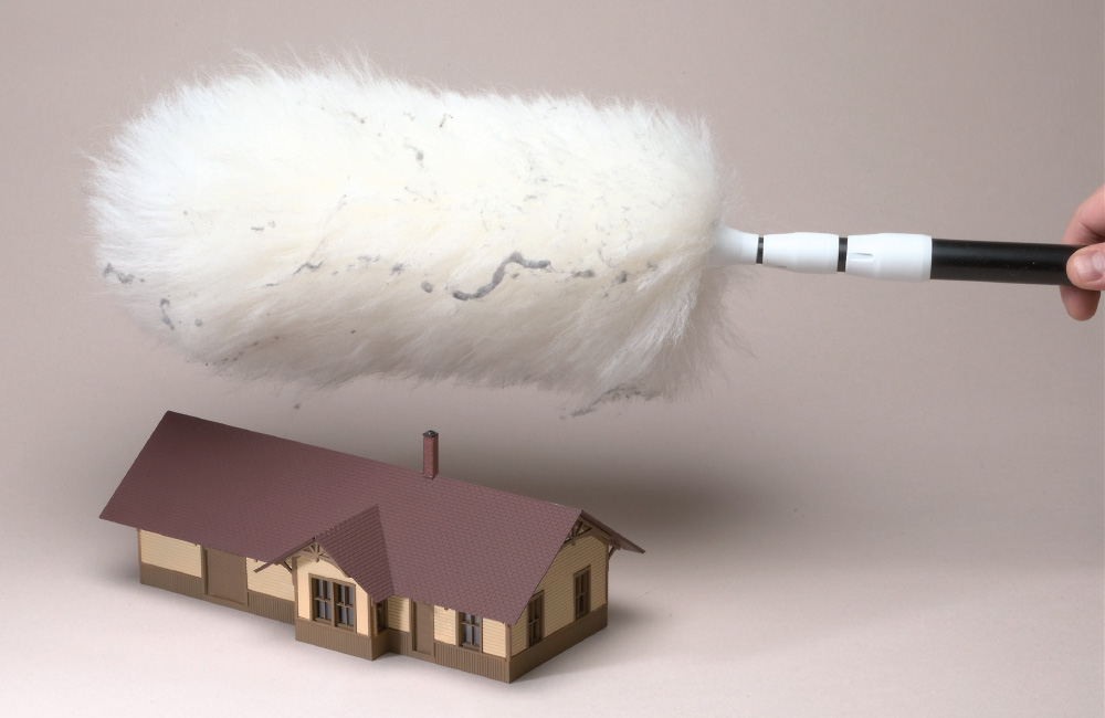 A hand holds a white duster with cobwebs on it above a model depot
