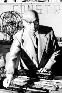 A black-and-white photo of a man standing behind a toy train layout