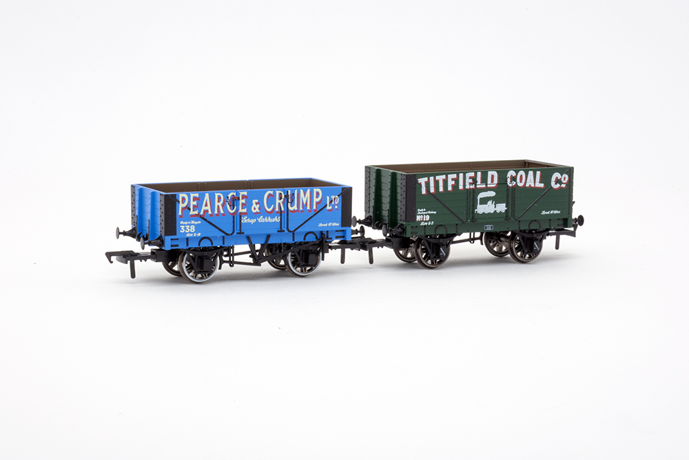 Rapido Trains UK Titfield Thunderbolt-inspired wagon 3-pack: Small British open-topped model train freight cars in bright blue and dark green with black and white bold lettering on them sitting on a blank white background.