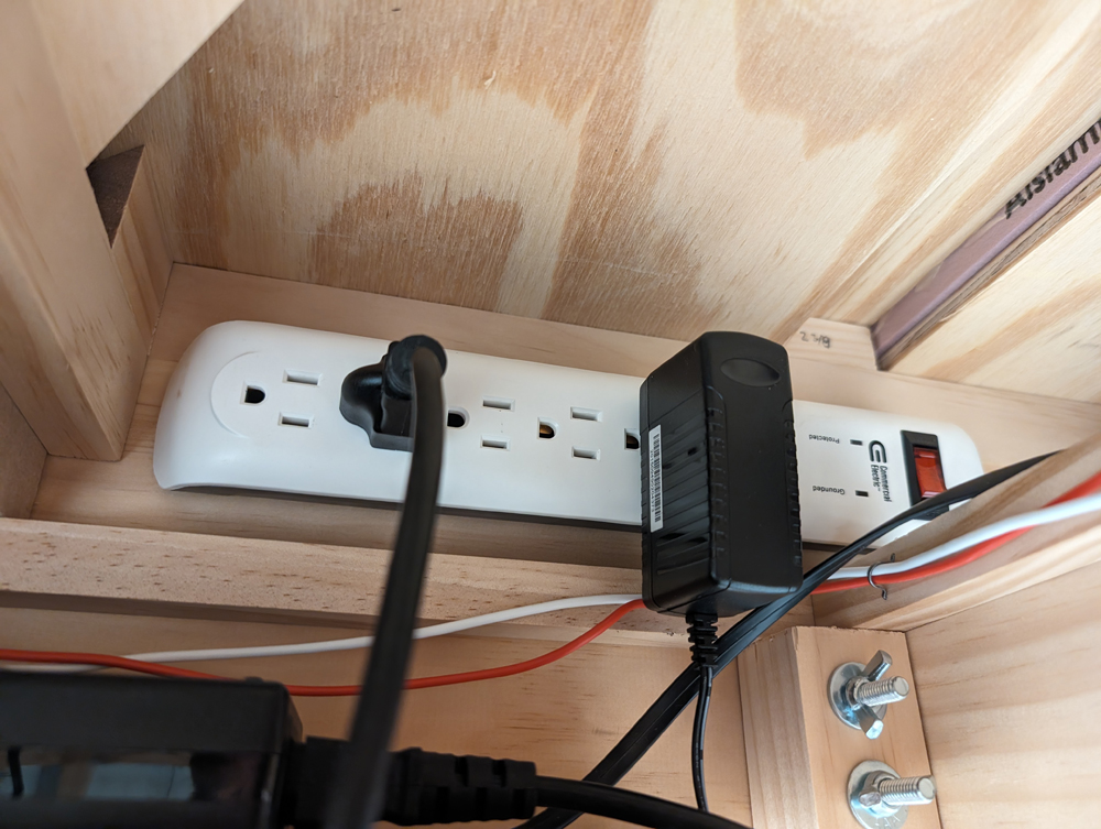 A surge protector power strip under a train layout with two devices plugged in.