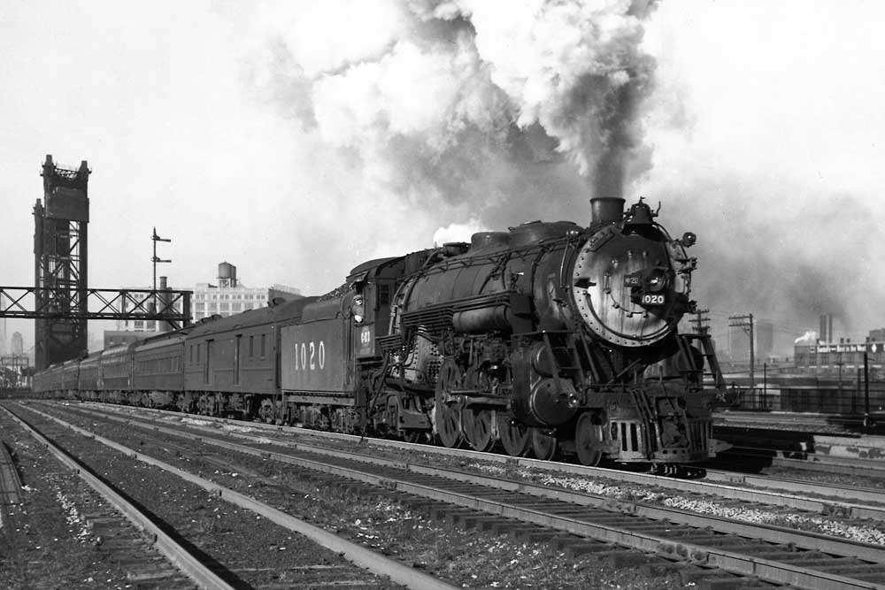 Smoking steam locomotive with passenger train under signal bridge